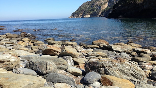 Une côte rocheuse parsemée de gros blocs et offrant une vue dégagée sur la mer et les falaises lointaines.