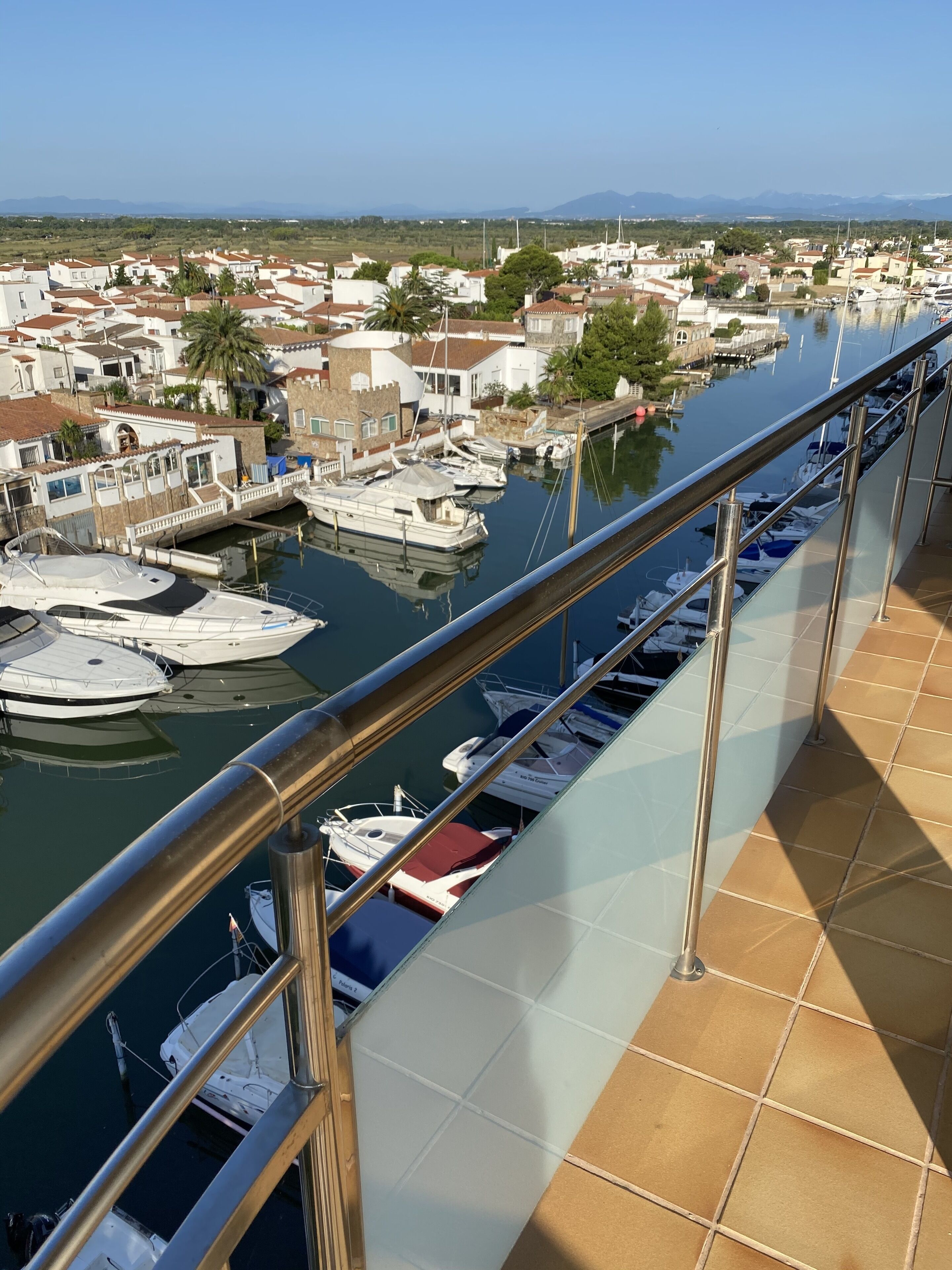 A marina with boats docked, a clear view of the surrounding town, and a balcony with a railing.