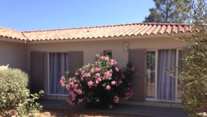 Una casa con tetto in tegole, un grande arbusto con fiori rosa e un cielo azzurro intenso.