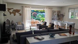 Un soggiorno moderno con divano, tavolino e zona pranzo con sedie. C'è una TV montata a parete, una decorazione raffigurante una mappa del mondo e una finestra con tende.