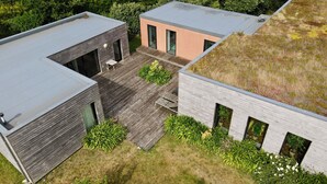Ein modernes Gebäude mit flachem Dach, einer Holzterrasse und umgebender Bepflanzung.