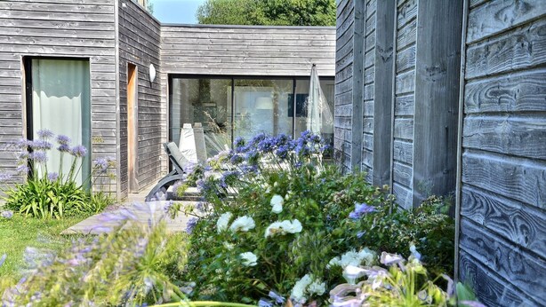 Ein modernes Gebäude mit Holzverkleidung, einer Glastür und einem Garten mit verschiedenen Pflanzen und Blumen.