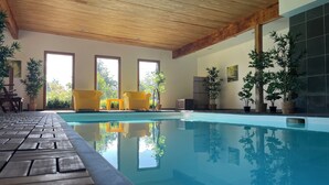 Ein überdachter Swimmingpool mit Holzboden, gelben Stühlen und Topfpflanzen.