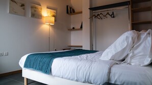 Ein Schlafzimmer mit einem Bett, einer Nachttischlampe, einem Kleiderschrank mit Kleidung und einem Regal mit Büchern.