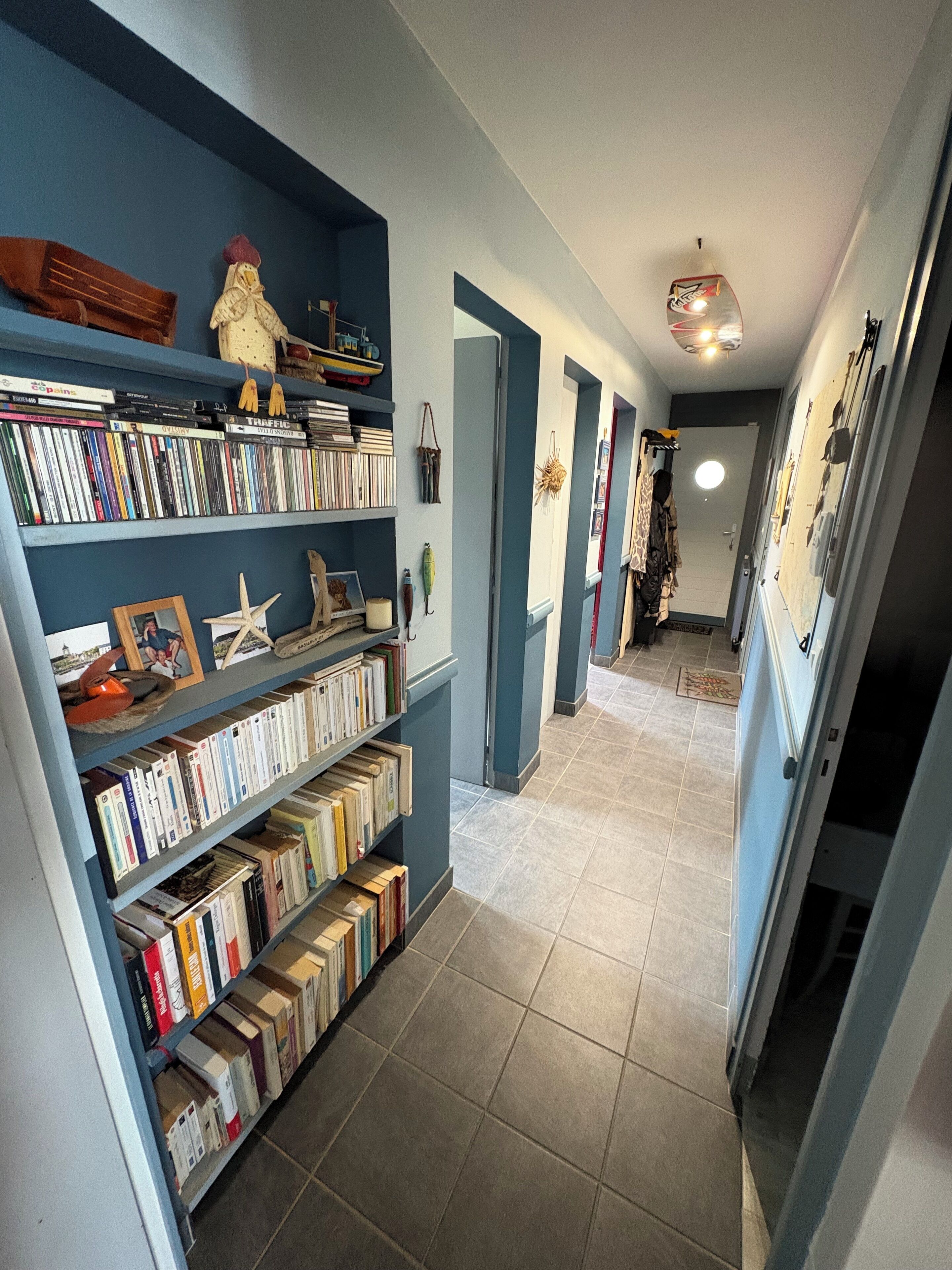 A hallway with a bookshelf filled with books and decorative items, leading to a room with a bed and a dresser.
