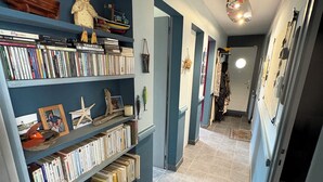 Un pasillo con una estantería llena de libros y objetos decorativos, que conduce a una habitación con cama y cómoda.