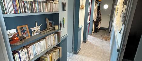 A hallway with a bookshelf filled with books and decorative items, leading to a room with a bed and a dresser.