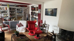 Una sala de estar acogedora con chimenea, un sillón rojo, una estantería y un cuadro en la pared.