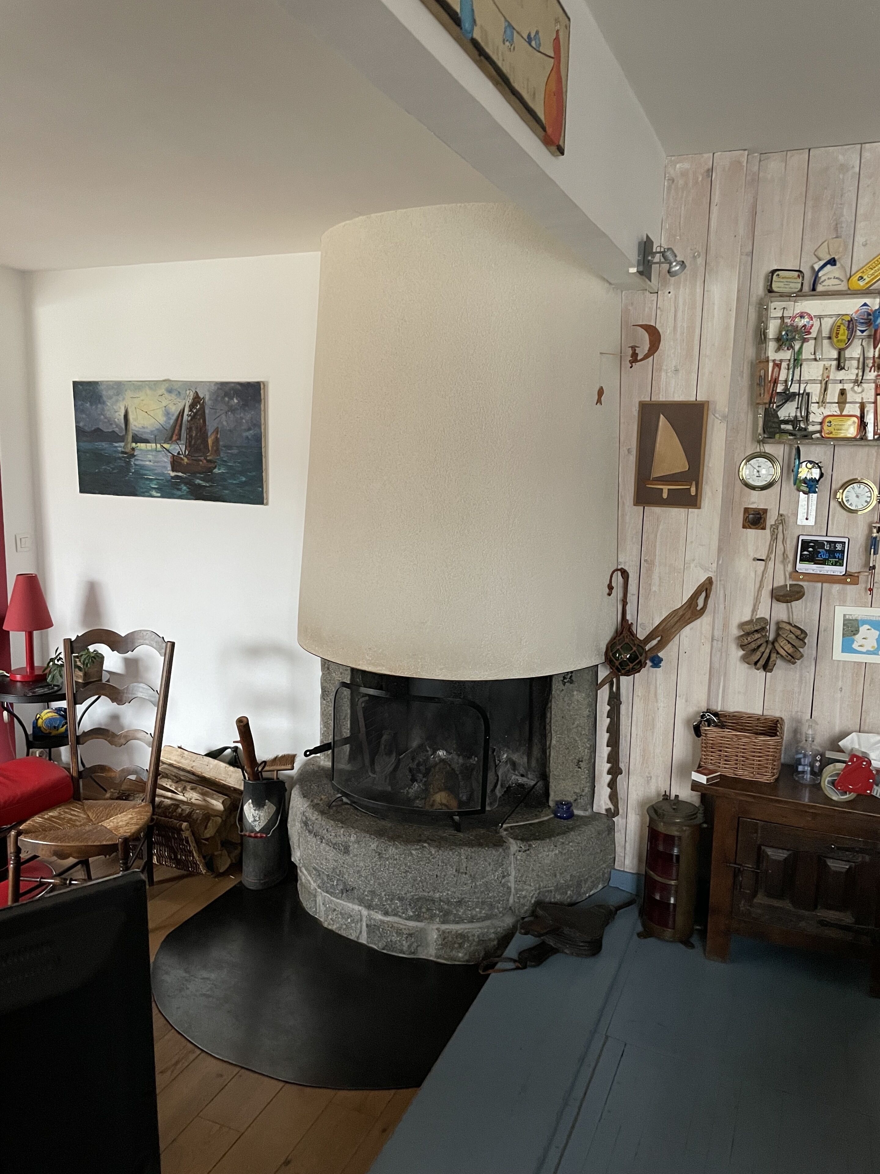 A cozy living room with a stone fireplace, a painting of sailboats, and a wall clock.