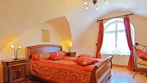 Ein Schlafzimmer mit einem hölzernen Bett, einem Nachttisch, einer Lampe und einem Fenster mit Vorhängen.
