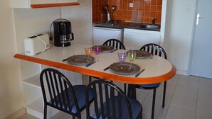 A compact kitchen with a microwave, toaster, and coffee maker. There are four chairs around a small dining table with plates, glasses, and cutlery. - Studio cabin Banyuls 4 pers, sea view, parking, WiFi (Banyuls-sur-Mer)