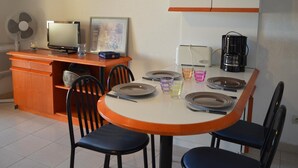 A dining area with a round table, chairs, a television, a fan, and a coffee maker. - Studio cabin Banyuls 4 pers, sea view, parking, WiFi (Banyuls-sur-Mer)