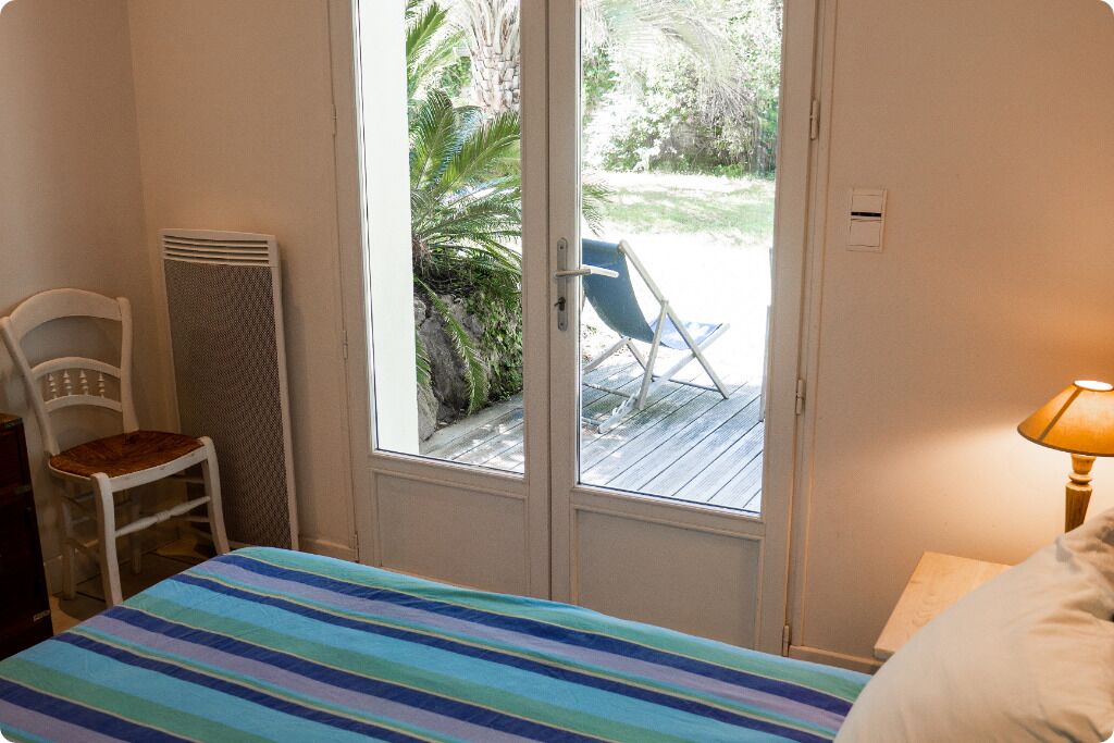 Un dormitorio con cama, una silla, un calentador y vistas a una terraza y palmeras.
