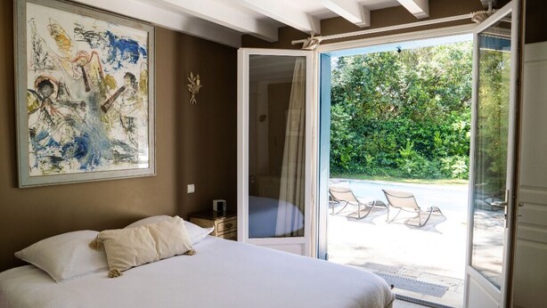 Un dormitorio con cama, un cuadro grande y un ventanal corredero que da a un área de estar al aire libre.