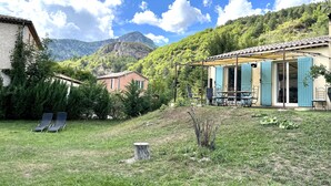 Una casa rústica con un patio, mobiliario exterior y montañas al fondo.