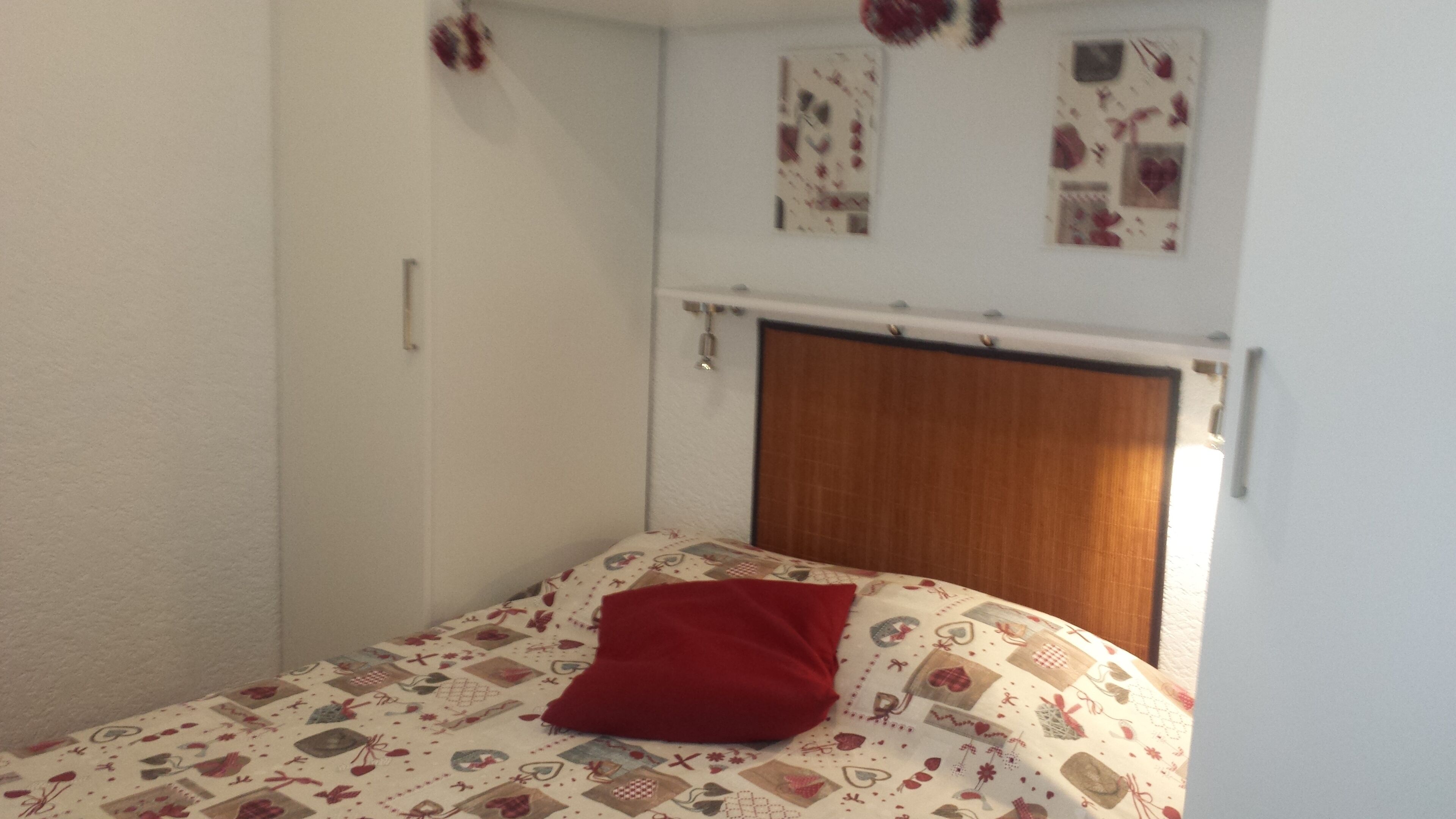 A bedroom with a bed, a red pillow, a wooden headboard, and a wall with a curtain.