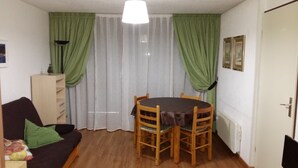 Ein kleiner, möblierter Raum mit einem runden Tisch, vier Stühlen, einer Couch, einem Schrank und einer Tür.