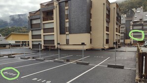 Ein Parkplatz mit markierten Stellplätzen und ein Mehrgeschosshaus mit Balkonen.