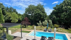 Una piscina rectangular con solárium empedrado, rodeada de sillones de descanso y una pérgola.