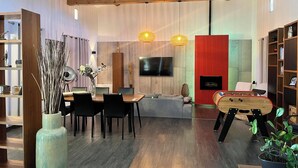 Una sala moderna con techo de madera, un comedor con mesa y sillas, chimenea y televisor montado en la pared.