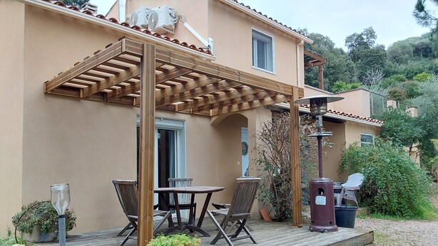 A covered patio area with a table and chairs, a trash bin, and a potted plant.