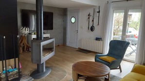 A living room with a wood-burning stove, a television, a blue armchair, and a yellow sofa.