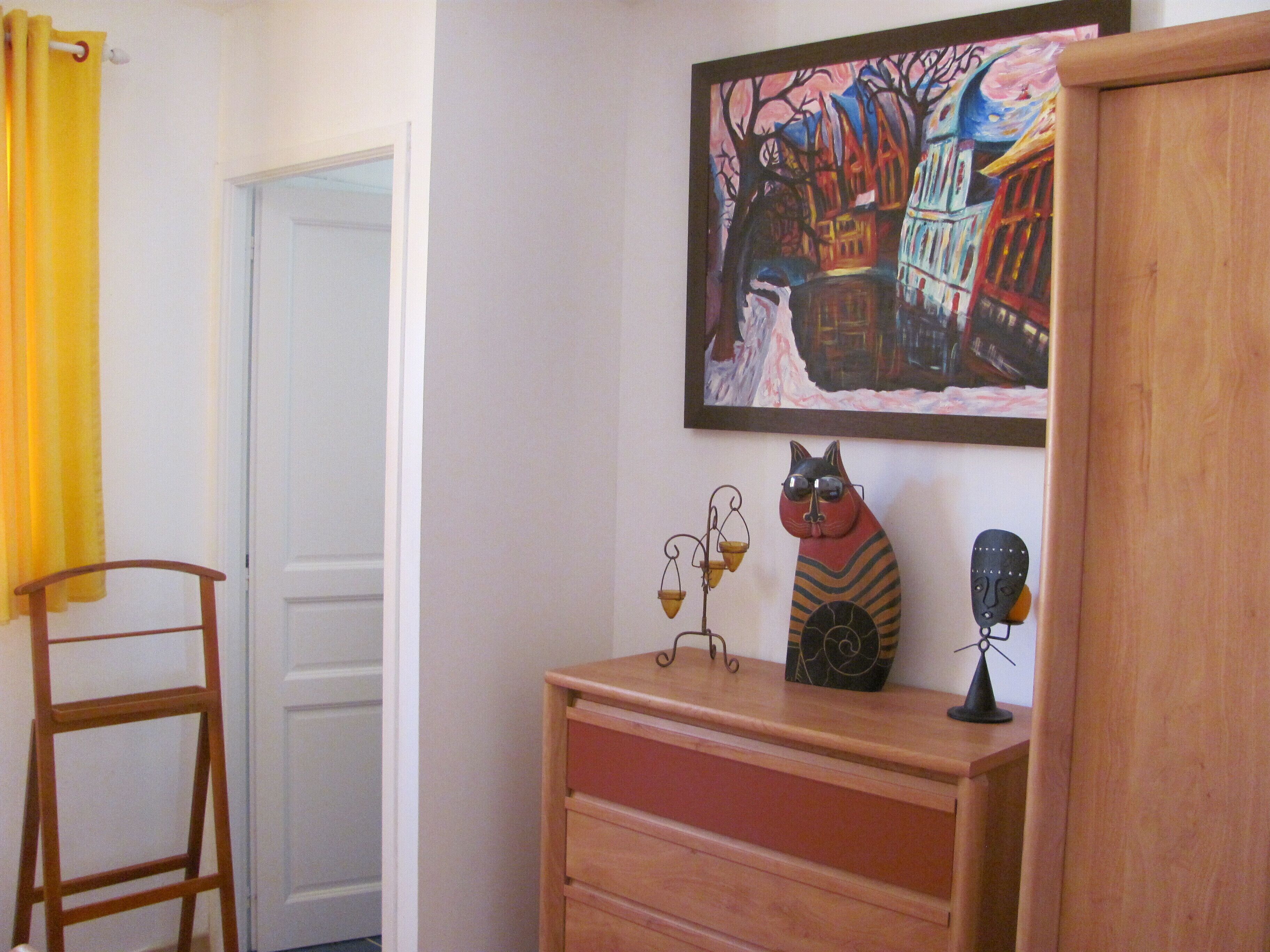 Una habitación con un aparador de madera, un cuadro de un paisaje invernal, una figurita de gato y una escalera.