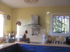 Cozinha com pia, fogão e diversos utensílios. Há uma janela com vista para o verde lá fora.
