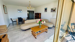 Un salón con un sofá, una mesa de centro con un florero, una zona de comedor con una mesa y sillas, y una araña.