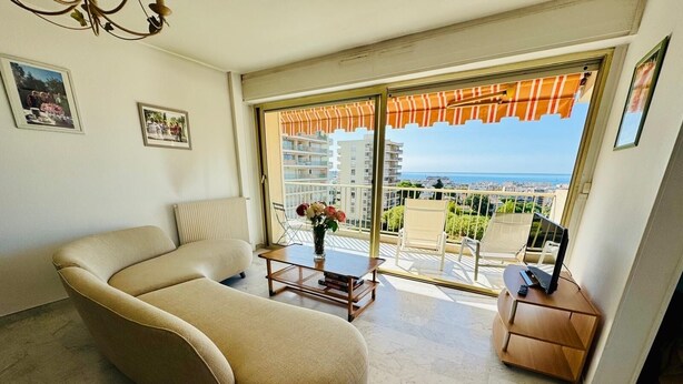 Una sala de estar moderna con un sofá curvo, una mesita con un florero y un balcón con vistas a la ciudad y al mar.
