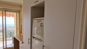 Una cocina con armarios blancos, un refrigerador y un ventanal corredero que da a un balcón.