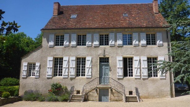 A two-story building with a symmetrical facade, white shutters, and a central entrance with a staircase.