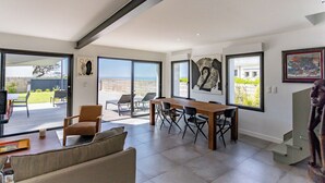 Un espacio habitable amplio con una mesa grande y sillas, un sofá y una estatua. Amplias ventanas ofrecen vistas al exterior.