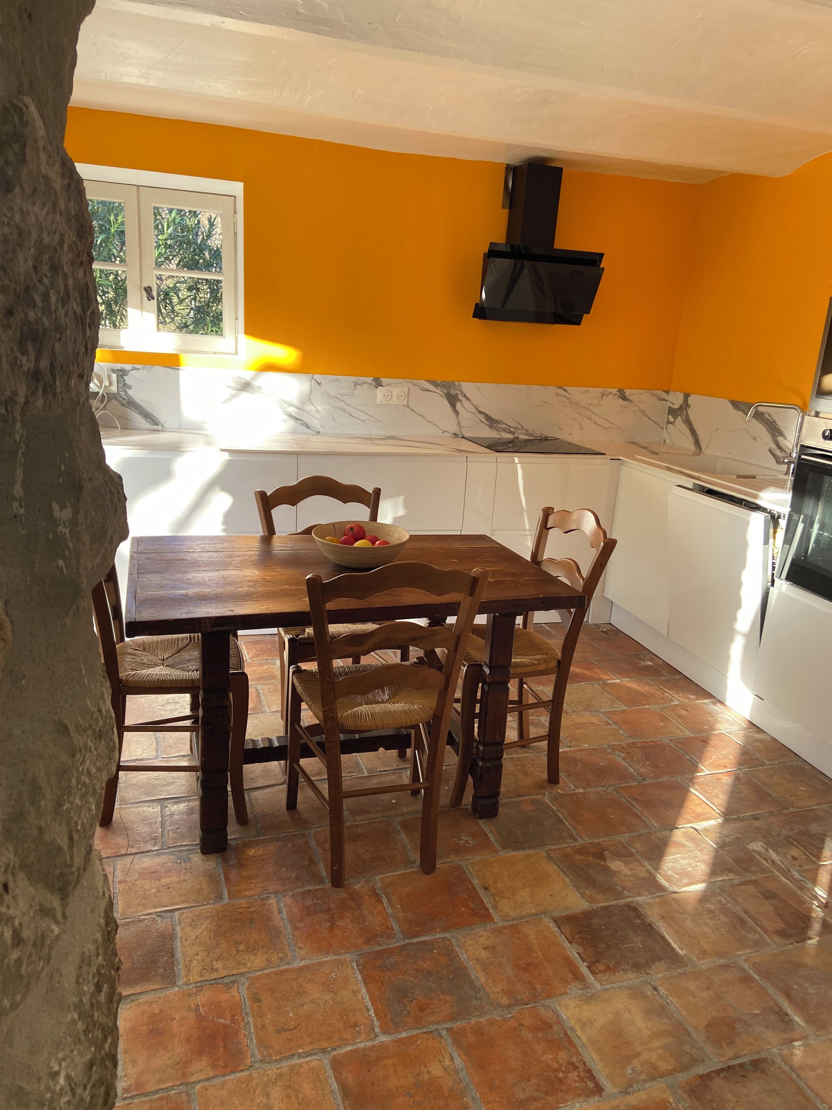 A kitchen with a dining table, chairs, and a bowl of fruit.