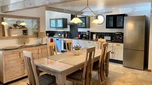 Una cocina moderna con armarios de madera, un refrigerador de acero inoxidable y un comedor con mesa y sillas de madera.