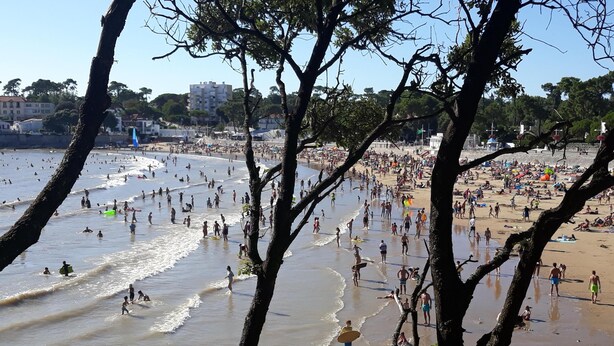 Uma praia cheia de gente aproveitando o mar e o sol.