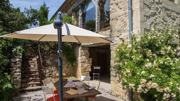 Una terrazza esterna con tavolo e sedie, un ombrellone grande e un edificio in pietra sullo sfondo.