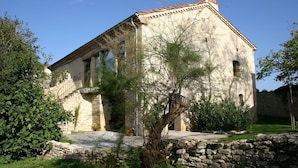 Un edificio in pietra con tetto in tegole, una scala che conduce a una porta e un muro in pietra di fronte.
