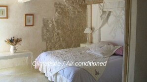 Una camera da letto con parete in pietra, un letto con biancheria bianca, un comodino con una lampada e un vaso con fiori.