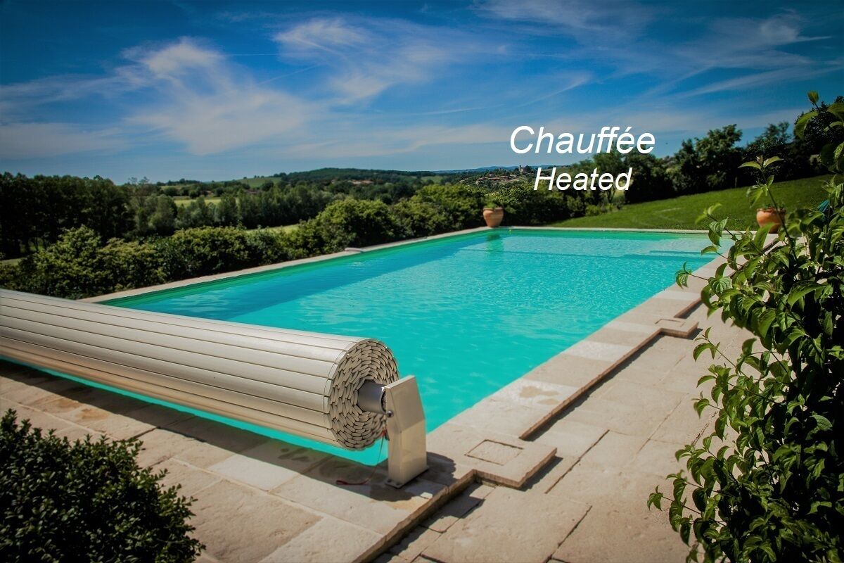 Une piscine extérieure chauffée, avec un ciel bleu dégagé et une végétation luxuriante en arrière-plan.