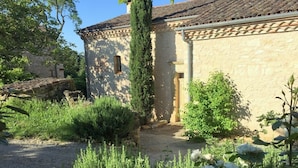 Un cortile con un edificio in pietra, un albero alto e vegetazione rigogliosa.