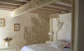 Ein Schlafzimmer mit Steinwand, einem Bett mit weißer Bettwäsche, einem Nachttisch mit Lampe und einer Vase mit Blumen.