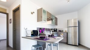 A modern kitchen with a built-in microwave, a stainless steel refrigerator, and a small dining area with two chairs. - New air-conditioned T2/3 MINI loft near the paradisiacal beaches of the South Shore (Grosseto-Prugna)