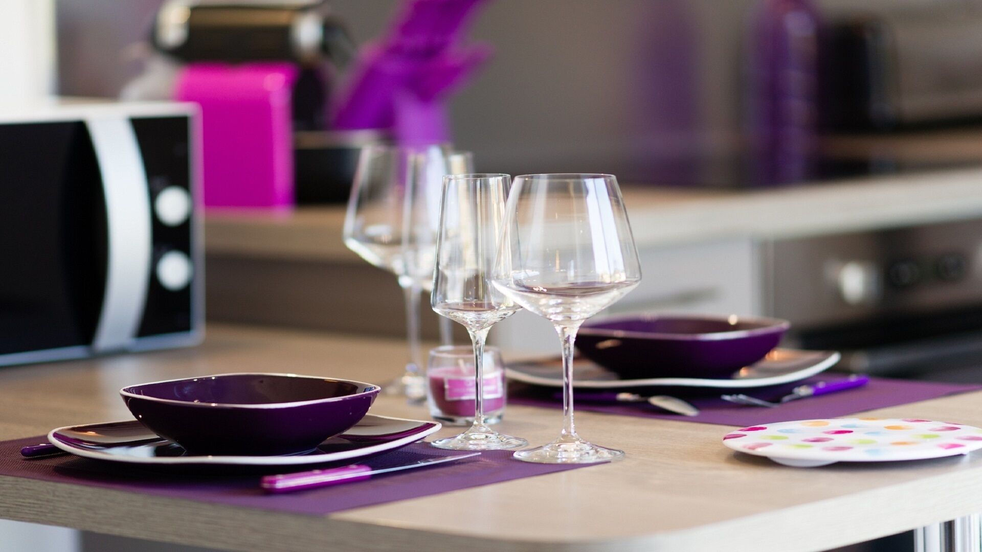 A dining table with purple placemats, clear wine glasses, and a purple bowl.
