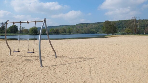 A sandy beach with a swing set and a lake in the background. - Typical cottage in Normandy Campaign (Plasnes)