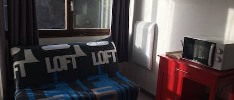 Quarto com cama, um armário vermelho, radiador branco e janela com cortinas.