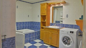 A bathroom with a checkered floor, a washing machine, a sink, and wooden cabinets.