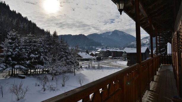 A wooden balcony with a view of a snowy landscape, including trees and buildings.