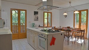 A kitchen with a central island, wooden cabinets, a stove, and a dining area with chairs and a table.