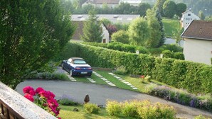 A residential area with a blue car parked on a driveway, surrounded by lush greenery and a well-maintained garden. - House for rent in the Haut Jura (Longchaumois)